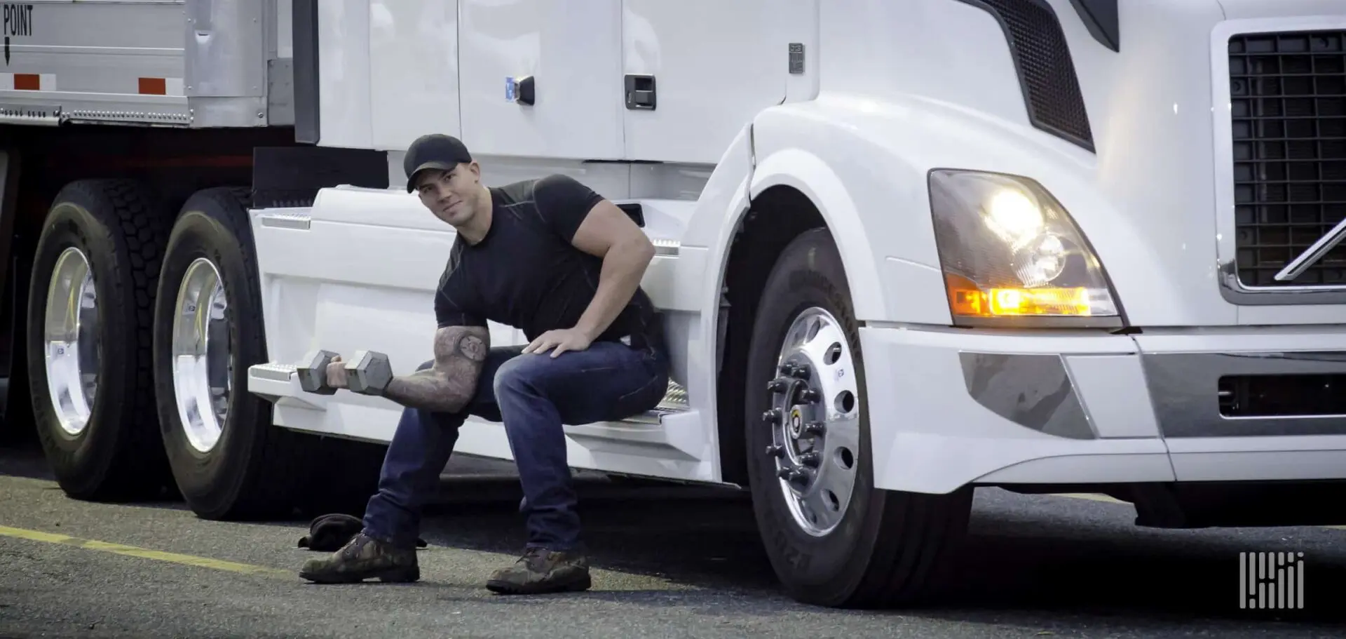 Man lifting weights by a semi-truck.