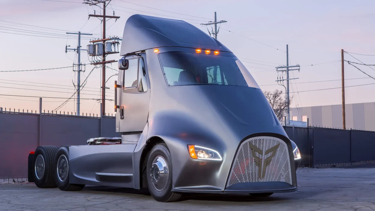 A gray semi-truck parked in front of a fence.