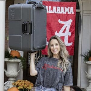 Woman holding a cooler in front of Alabama flag.