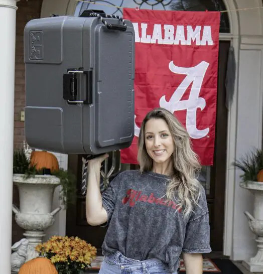 Woman holding a cooler in front of Alabama flag.